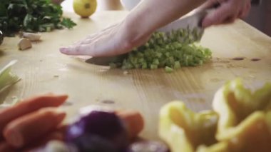 Genç bir kadın aşçının ev mutfağındaki hafif ahşap çalışma masasında çeşitli sebzelerle kereviz keserken düşük açılı görüntüsü Akdeniz mutfağındaki günlük yaşam anları.