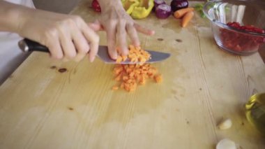 Genç bir kadın aşçının havuç keserken ve ev mutfağındaki açık ahşap çalışma masasında cam bir kaseye koyarken düşük açılı görüntüsü Akdeniz mutfağında günlük hayatın anlarını yansıtıyor.