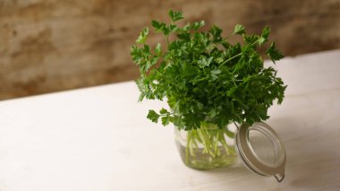 Mutfakta yeşil maydanozlu su dolu açık cam bir kavanozun kapağını aç. Hafif ahşap arka plan, Akdeniz mutfağı.