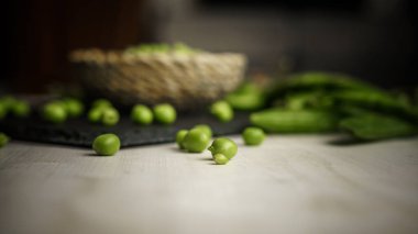 Ön planda taze kabuklu bezelyenin alt açısını kapatın ve siyah tahta tabakta bir sepet dolusu ve bokeh efektli hafif ahşap arka planda kabuklar. Sağlıklı yeşil kopyalama alanı