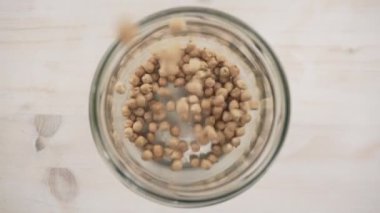 Ağır çekimde yukarıdan aşağıya cam kavanoza düşen nohut manzarası, temel sağlıklı vegan yemek teması