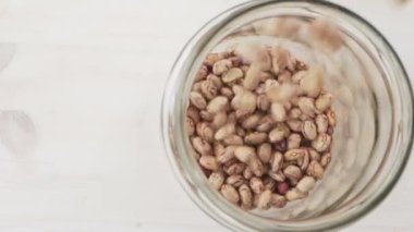 Ağır çekimde yukarıdan aşağıya, sıradan fasulyelerin cam kavanoza düşüşünü, basit sağlıklı vejetaryen yemek konsepti temasını.