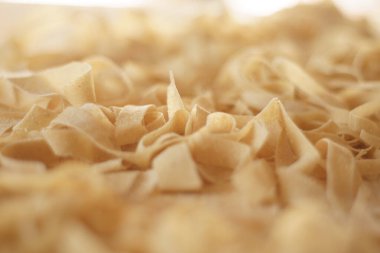 Taze ev yapımı makarna hazırlanıyor: Makro yakın çekim el yapımı taze tagliatelle bokeh efektiyle sarılmış ve kesilmiş.