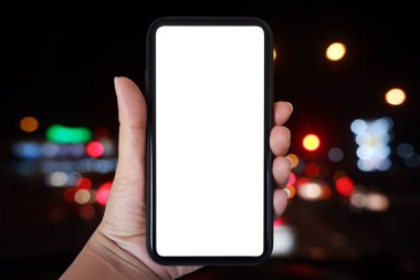 Yakın plan sol el telefonu dikey tutuyor, gece arkaplanındaki bulanık trafik ışığına doğru akıllı telefon kullanıyor - boşluğu kopyala.