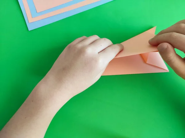 Origami step by step. How to make a paper bunny for Easter greetings and fun. DIY concept. Top view of kids hands making papercraft. Step by step photo instruction 5 out of 11.