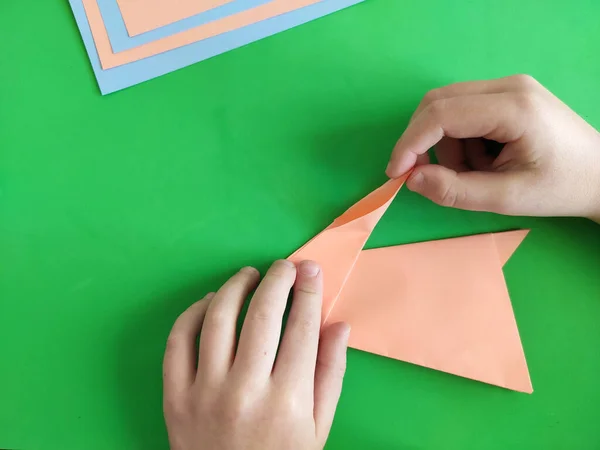 Origami step by step. How to make a paper bunny for Easter greetings and fun. DIY concept. Top view of kids hands making papercraft. Step by step photo instruction 10 out of 11.