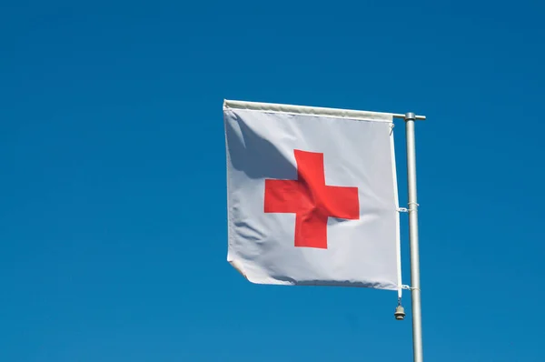 The flag of International Red Cross and Red Crescent Movement against a blue sky in Manno, Switzerland. The Red Cross is an international humanitarian movement with approximately 97 million volunteers