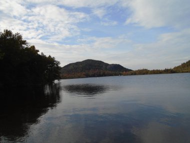 Başında bulutlu bir gökyüzü olan sakin bir gölün yansıması.
