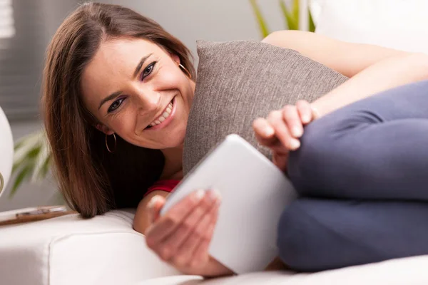 Uśmiechnięta kobieta z tabletem na jej kanapie — Zdjęcie stockowe