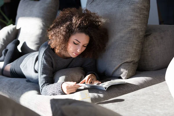 Rik flicka läsa något på hennes soffa — Stockfoto