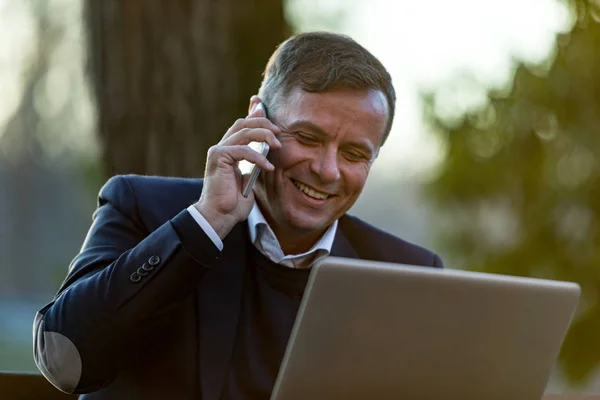 Uomo anziano con computer portatile e mobile all'aperto — Foto Stock