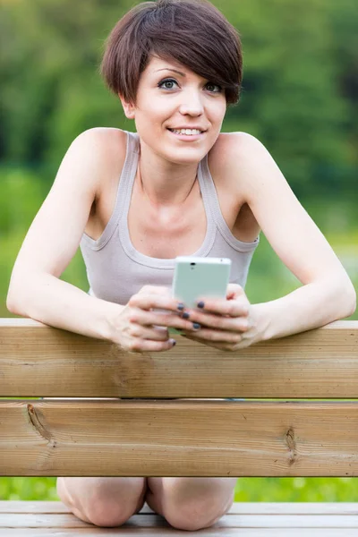 Mujer arrodillada en un banco con un móvil — Foto de Stock