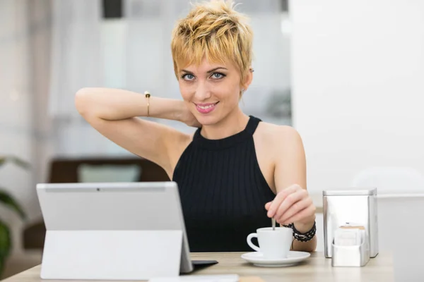 Γυναίκα ανάμειξη της καφέ ενώ χρησιμοποιώντας έναν υπολογιστή σε ένα μπαρ — Φωτογραφία Αρχείου