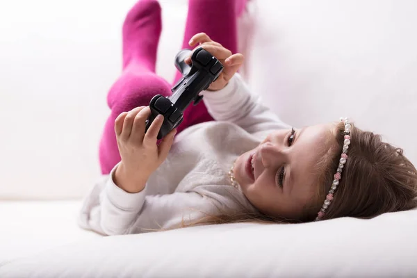 Little girl lying playing with a game controller — Stock Photo, Image