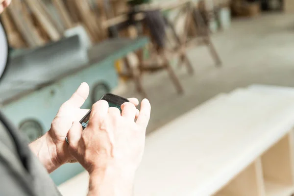 Handen van een schrijnwerker die met behulp van een mobiele — Stockfoto