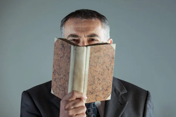 Senior man looking at camera behind an old book — Stock Photo, Image