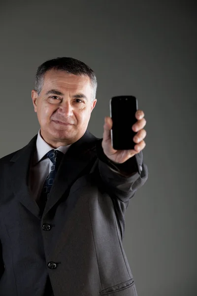 Serious businessman holding up a smartphone — Stock Photo, Image