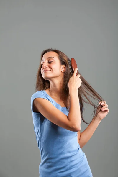 Mooie jonge vrouw haar lange bruine haren borstelen — Stockfoto