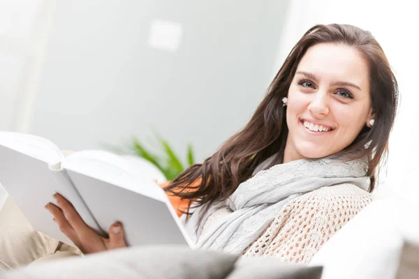 Ung kvinna håller en bok i soffan hemma — Stockfoto