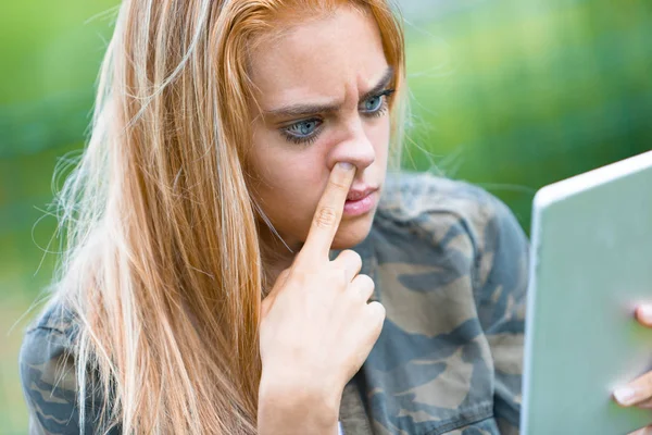 Девушка ковыряется в носу и смотрит планшет — стоковое фото