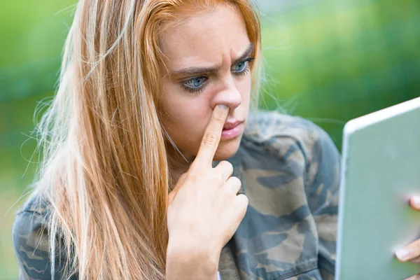 Flicka plocka näsan och titta på en tablett — Stockfoto