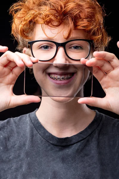 Sorriso de uma menina em aparelho através de um telefone móvel transparente — Fotografia de Stock