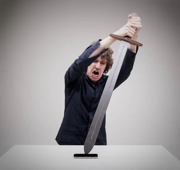 Angry man hitting his phone with a sword — Stock Photo, Image