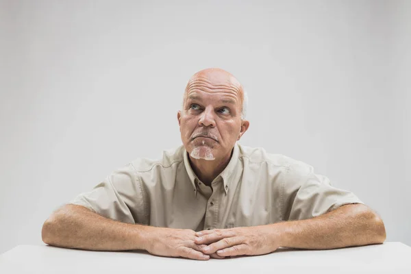 Doordachte oudere kalende man zit aan een tafel — Stockfoto