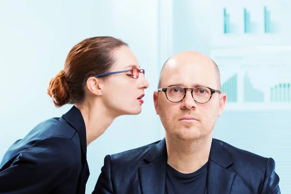 Женщина шепчет мужчине на ухо в офисе — стоковое фото