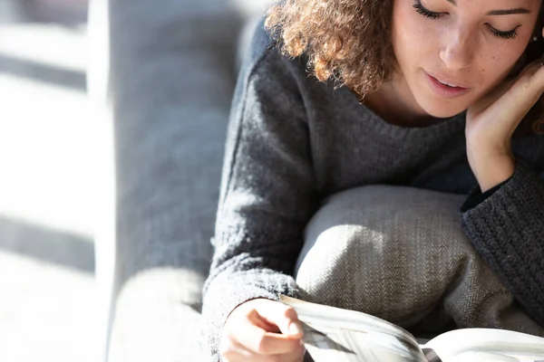 Hermosa Joven Morena Suéter Gris Tumbada Sofá Leyendo Una Revista — Foto de Stock