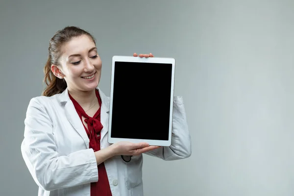 微笑友善的女医生或护士举着平板电脑 在灰蒙蒙的背景下给观众看 并留有复制空间 — 图库照片