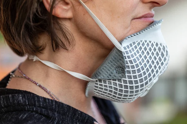 Woman wearing a face mask around her throat showing the wrong way to wear it as protection against the coronavirus or Covid-19 during the pandemic