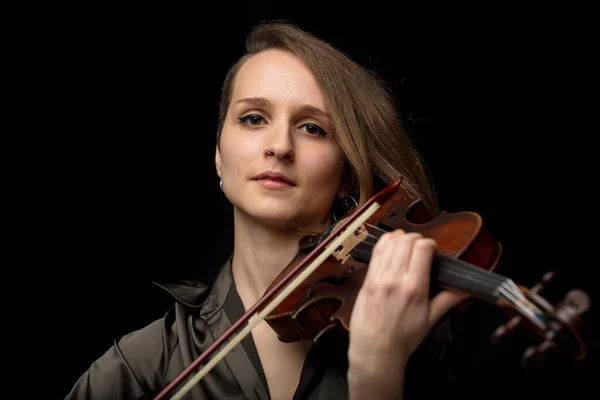 Serious young female violinist or musician playing on an antique Baroque violin during a classical music performance in a head and shoulders frontal portrait on black