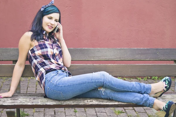 Jonge vrouw zittend op houten bankje in gesprek met de mobiele telefoon — Stockfoto
