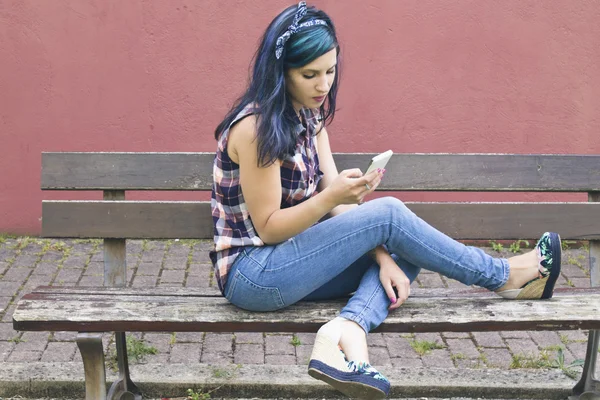 携帯電話に話している木製のベンチに座っている若い女性 — ストック写真