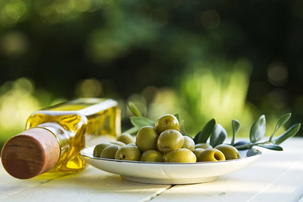 Plato de aceitunas y botellas de aceite sobre fondo verde — Foto de Stock