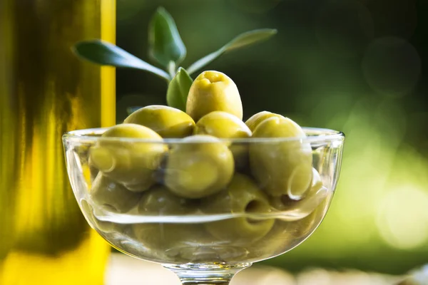 Glass cup filled with olives and olive oil bottles — Stock Photo, Image