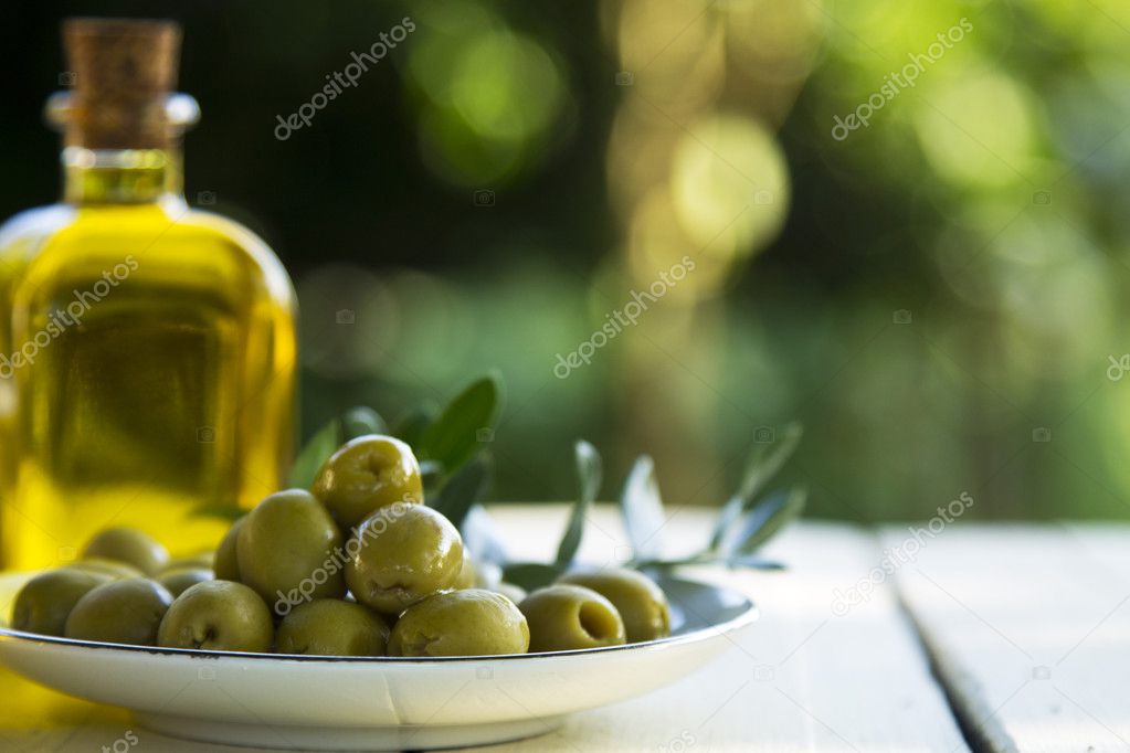 dish of olives and oil bottles on green background