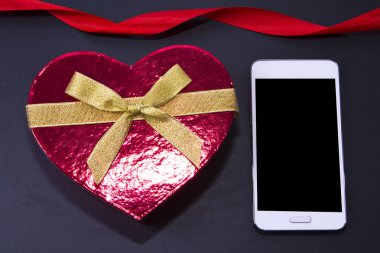 Kalp şeklinde hediye kutusu ve tahta arka plan üstünde hareket eden telefon