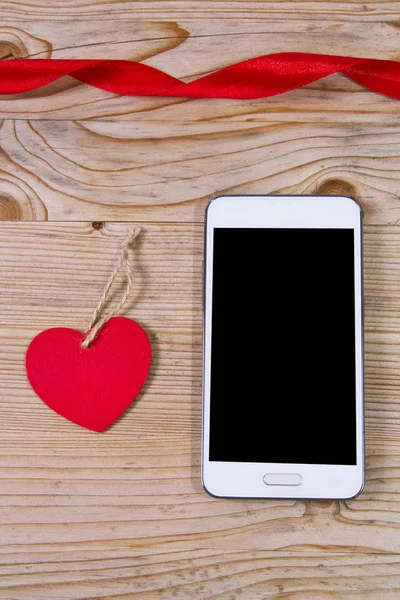 Heart-shaped tag and mobile phone on wooden background — Stock Photo, Image