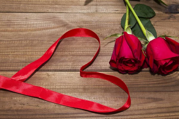 木製の背景にハートと赤いバラを描く赤いリボン — ストック写真