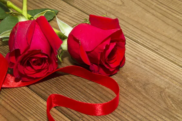 Red ribbon drawing a heart and red roses on wooden background — Stock Photo, Image