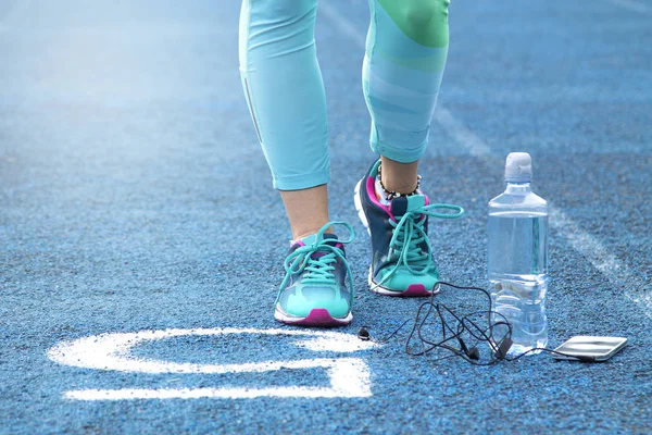 Mujer haciendo ejercicios en pista atlética con teléfono móvil — Foto de Stock