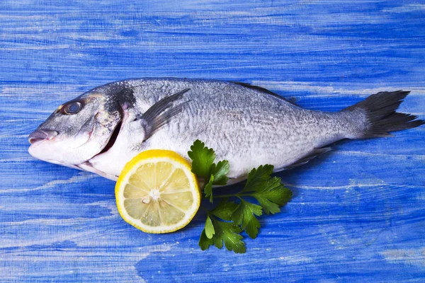 Ryba pražma s petrželkou a citronem na modré dřevěné pozadí — Stock fotografie