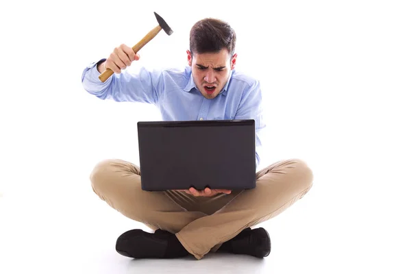 Mężczyzna siedzący na podłogę uderzając komputer z młotem — Zdjęcie stockowe
