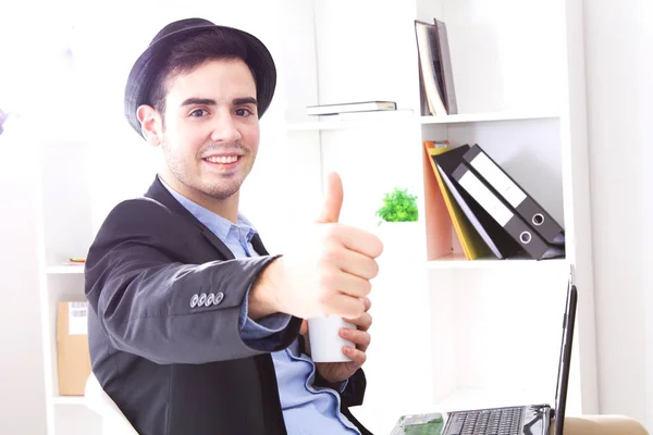 Чоловік сидить на роботі в офісі з комп'ютером, що має каву і робить нормальний жест — стокове фото
