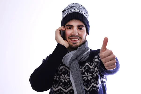 Молодий чоловік з светром і шарфом розмовляє на мобільному телефоні роблячи знак ОК — стокове фото