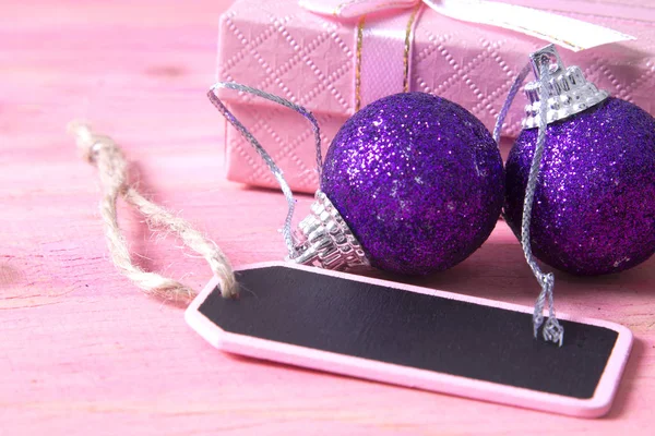 Christmas card with label, gift box and Christmas balls on pink background