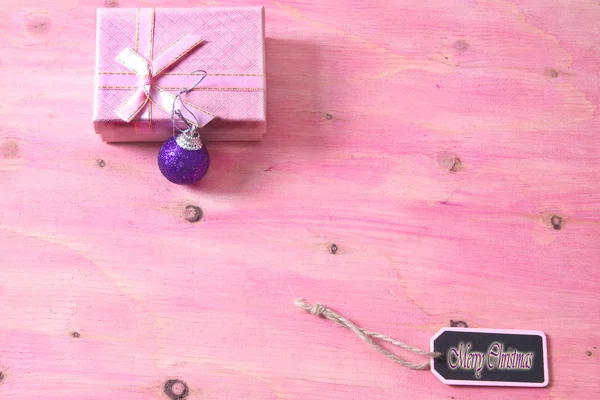Рождественская открытка с этикеткой, подарочной коробкой и рождественскими шарами на розовом фоне — стоковое фото