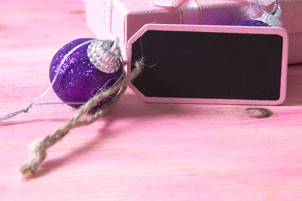 Cartão de Natal com etiqueta, caixa de presente e bolas de Natal no fundo rosa — Fotografia de Stock